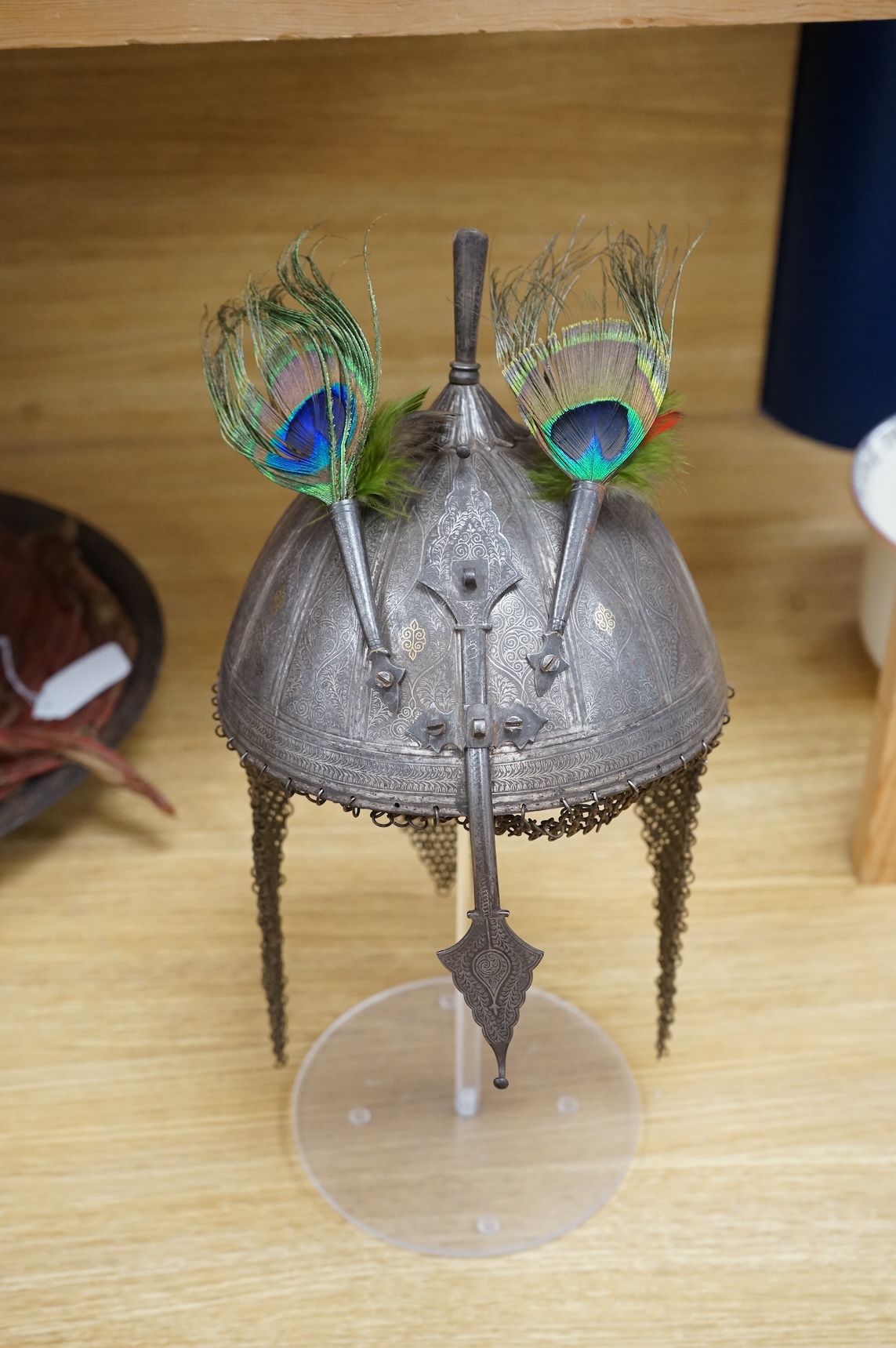 A mid to late 19th century Indian helmet and matching shield, covered with silver koftgari decoration, the helmet with sliding nasal bar and twin plume sockets surmounted by a third plume socket, the skull fluted like a